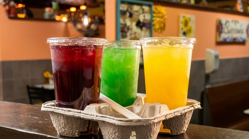 Three vibrant iced drinks in a cardboard carrier on a wooden counter.