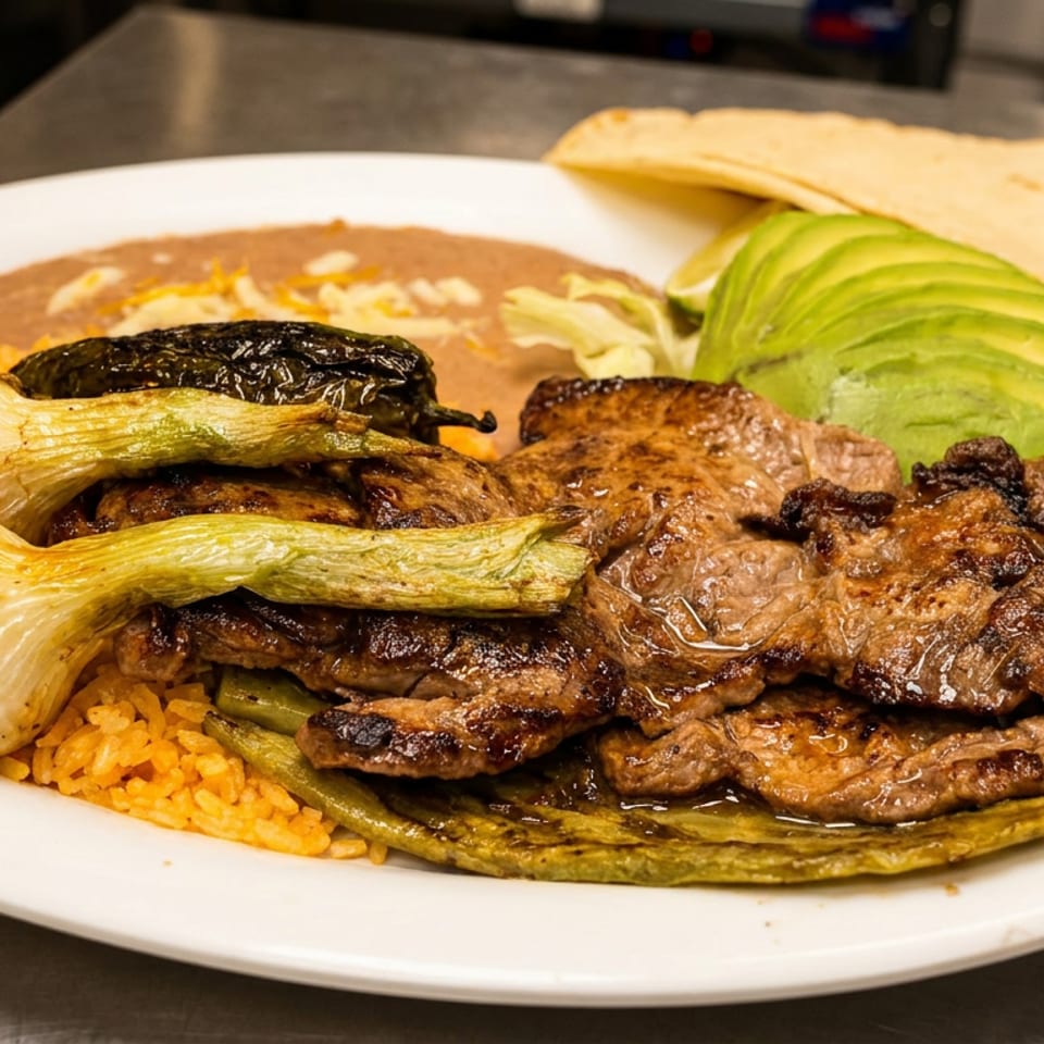 Grilled steak with rice, beans, avocado, grilled onions, and peppers on a white plate.