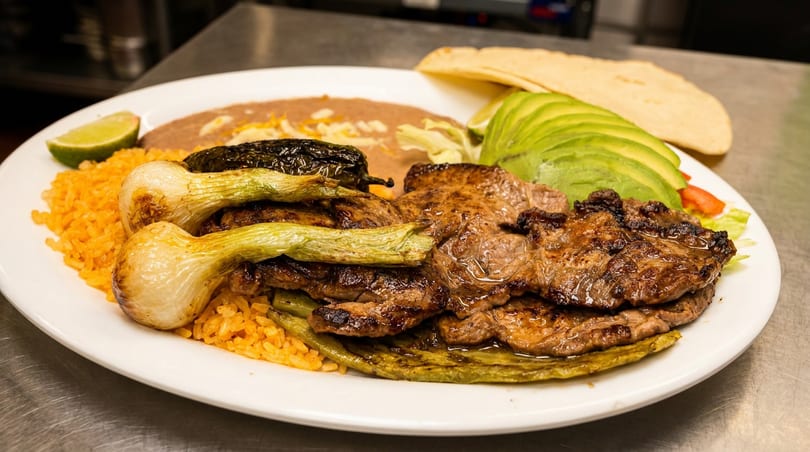 A vibrant Mexican platter featuring grilled steak, rice, beans, avocado, and grilled green onions.