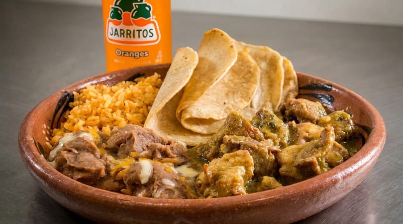 Mexican meal in a clay bowl with rice, beans, meat, tortillas, and an orange Jarritos soda.