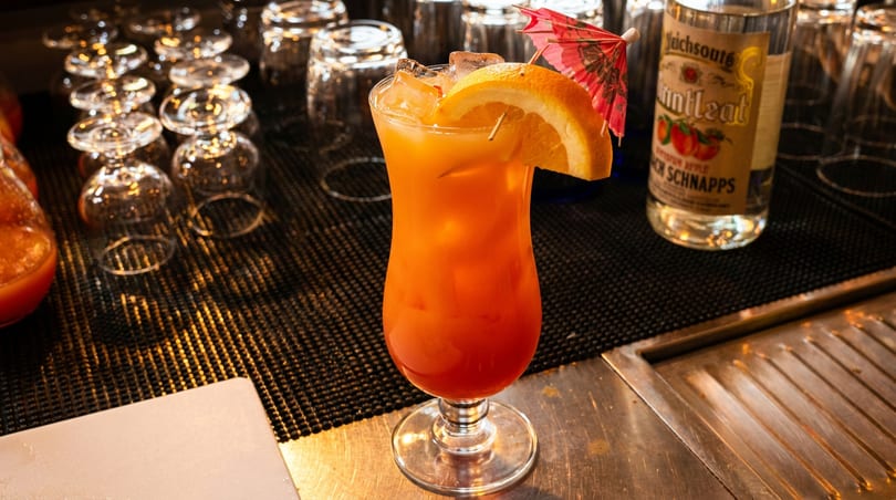 Tropical orange cocktail with an orange slice and umbrella on a bar counter.